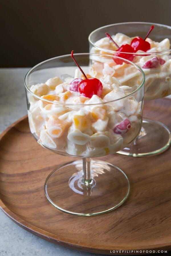 Filipino fruit salad topped with maraschino cherry served in stemmed glass.