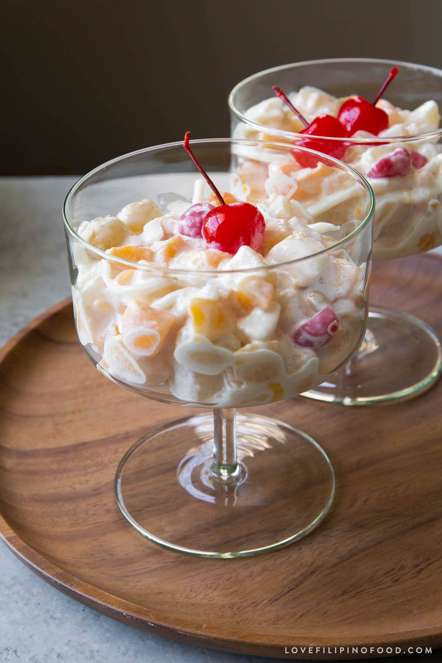 Filipino fruit salad topped with maraschino cherry served in stemmed glass.