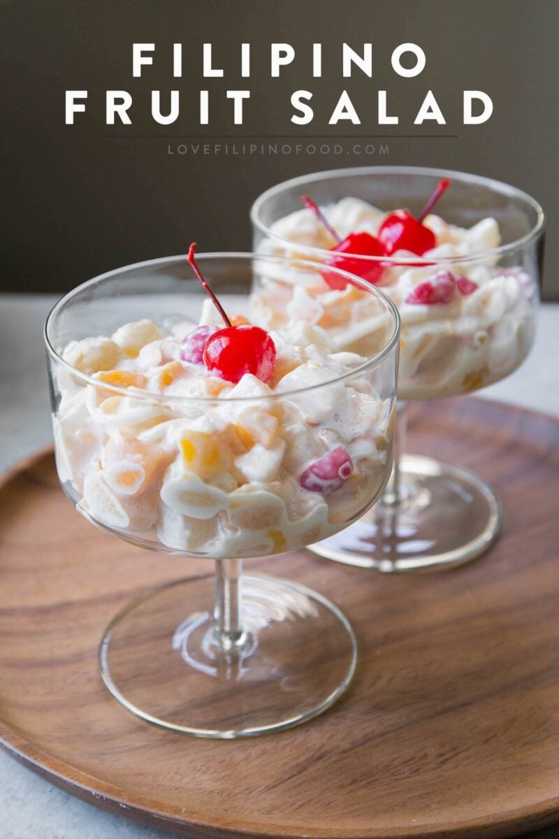 two stemmed glasses filled with filipino fruit salad topped with maraschino cherries.