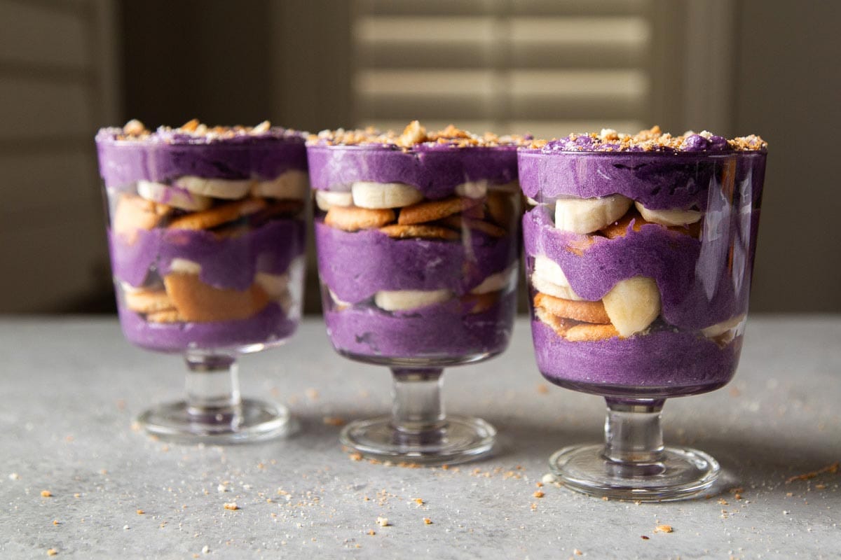three stemmed glasses of coconut ube banaa pudding parfaits in a row.