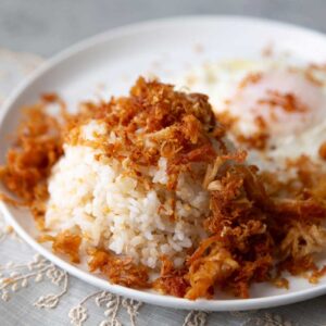 crispy chicken adobo flakes over rice on white plate.