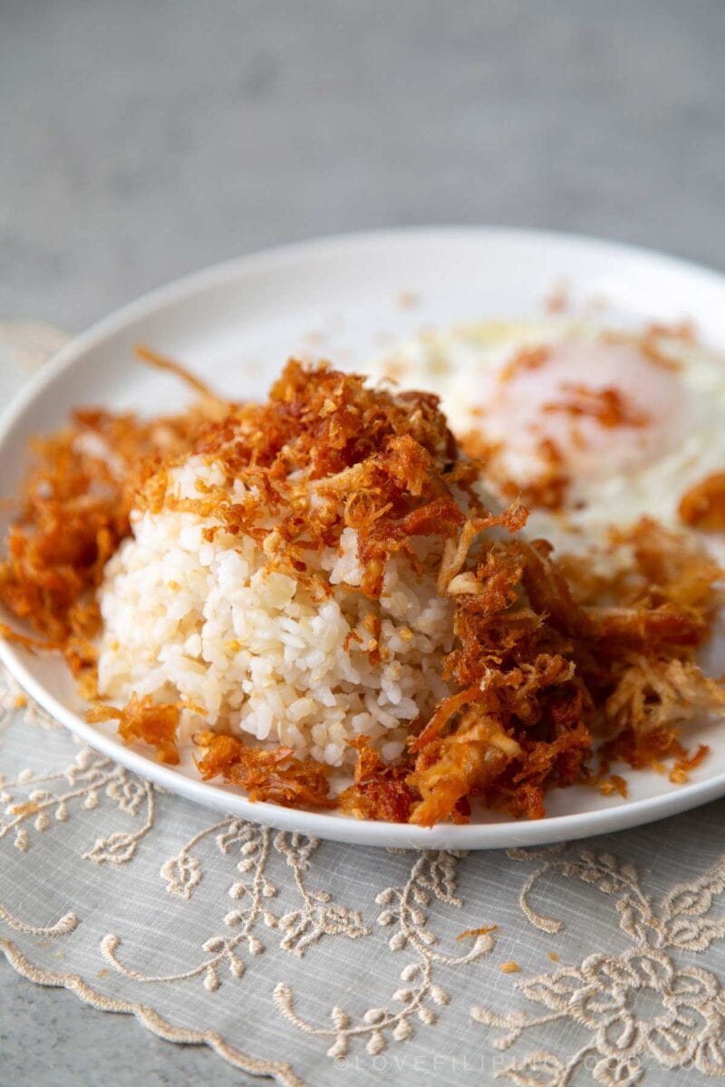 crispy chicken adobo flakes over rice on white plate.
