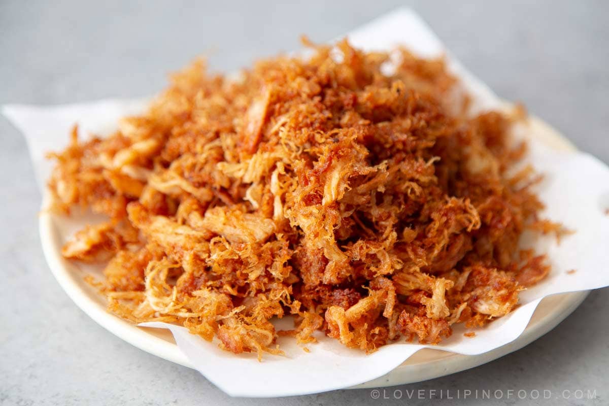 close up of crispy chicken adobo flakes piled on white plate.