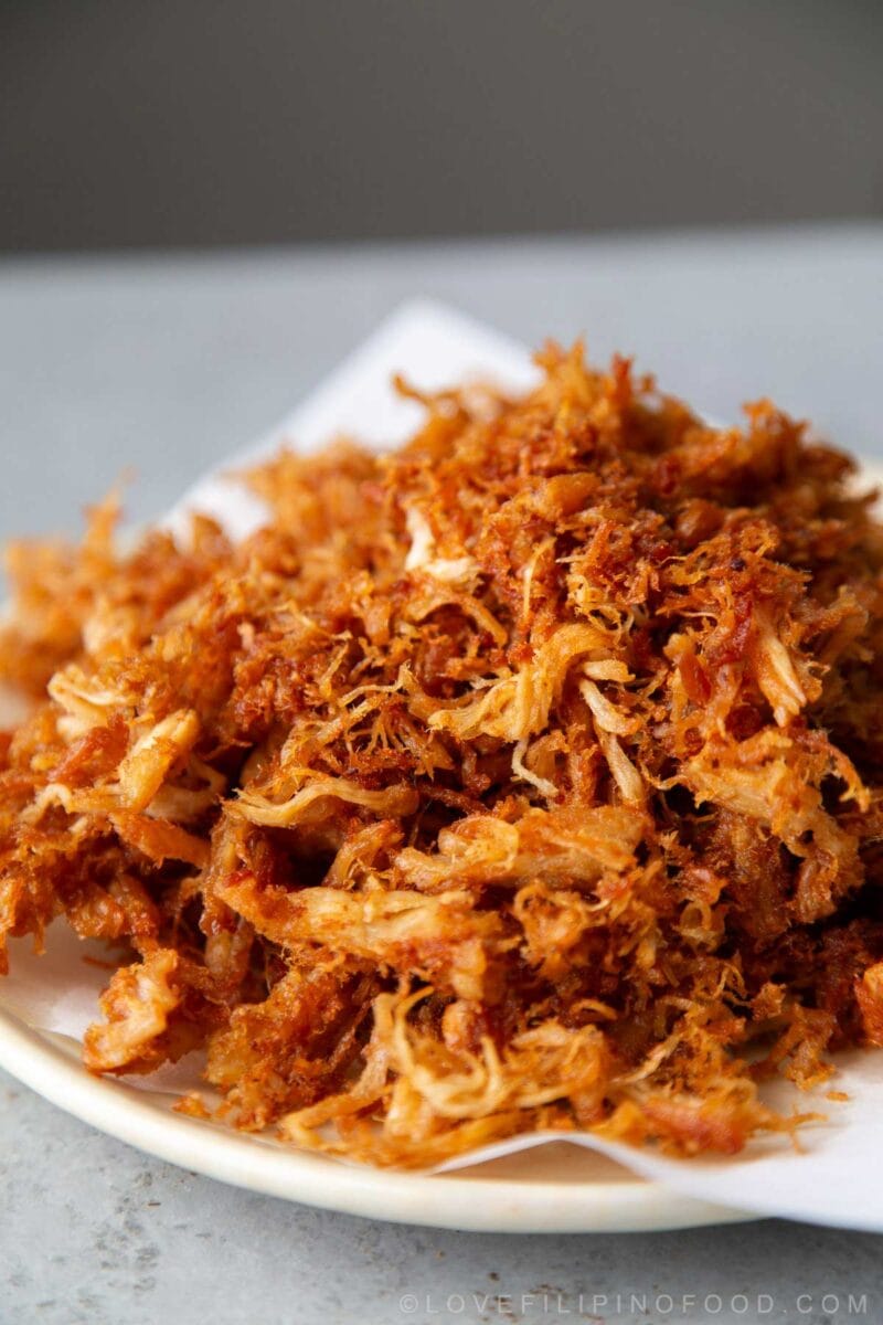 close up of crispy chicken adobo flakes piled on white plate.